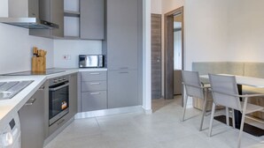 Une cuisine moderne avec des meubles gris, un four encastré et un coin repas comprenant une table et des chaises.
