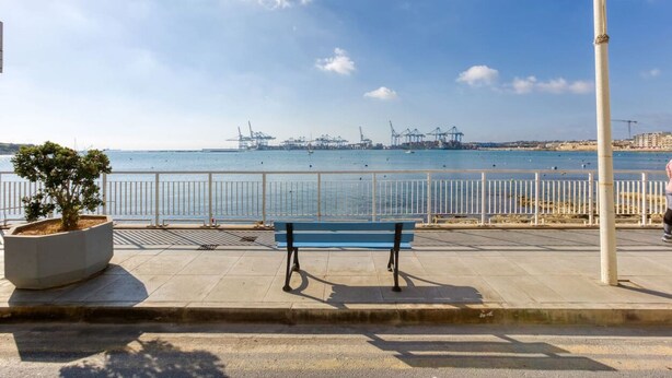 A waterfront promenade with a bench, a potted plant, and a pedestrian walkway.