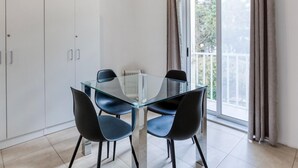 A modern dining area with a glass table and black chairs, white cabinets, and a large window with curtains. - Spacious, central APT in Paceville/St Julians (San Ġiljan)