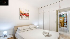A neatly arranged bedroom with a bed, bedside table, and a painting on the wall. - Spacious, central APT in Paceville/St Julians (San Ġiljan)