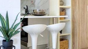 A modern kitchen with white marble backsplash, two white bar stools, a potted plant, and a wooden cabinet. - A lovely designer Apt with Balcony in St` Julians (St. Julian`s)