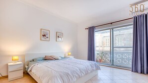 Une chambre avec un grand lit, deux tables de chevet avec des lampes, une fenêtre avec des rideaux et un balcon avec une balustrade.