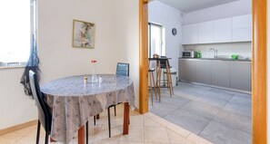 A dining area with a round table, chairs, and a vase of flowers. There is a kitchen in the background with cabinets and a microwave. - Stylish & Cosy 2BR Apt in the Heart of St` Julians (San Ġiljan)