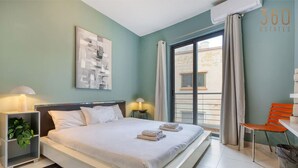 A hotel room with a bed, bedside tables, a chair, and a view of the outside. - Modern & private 1BR APT in the Heart of Paceville (St. Julian`s)