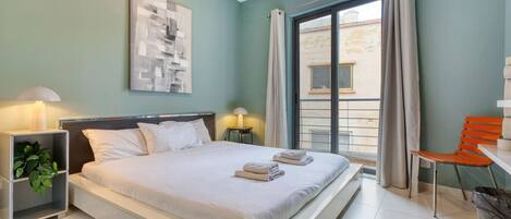 A hotel room with a bed, bedside tables, a chair, and a view of the outside.