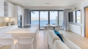 Una cocina moderna con una isla central, comedor con sillas y un sofá con vista al mar.