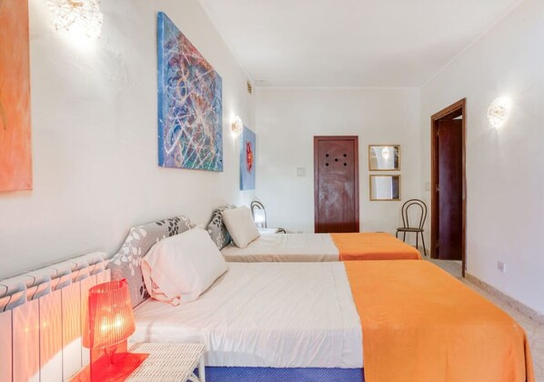 Una habitación con dos camas, una puerta de madera, una lámpara de pared y un cuadro.
