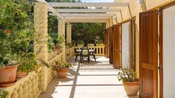 A covered outdoor area with a table and chairs, surrounded by potted plants and stone walls.