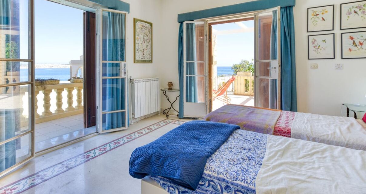 A bedroom with a bed, a view of the sea, and an open sliding door to a balcony.