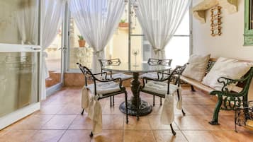 A dining area with a round table and chairs, a bench, and a view through a glass door.