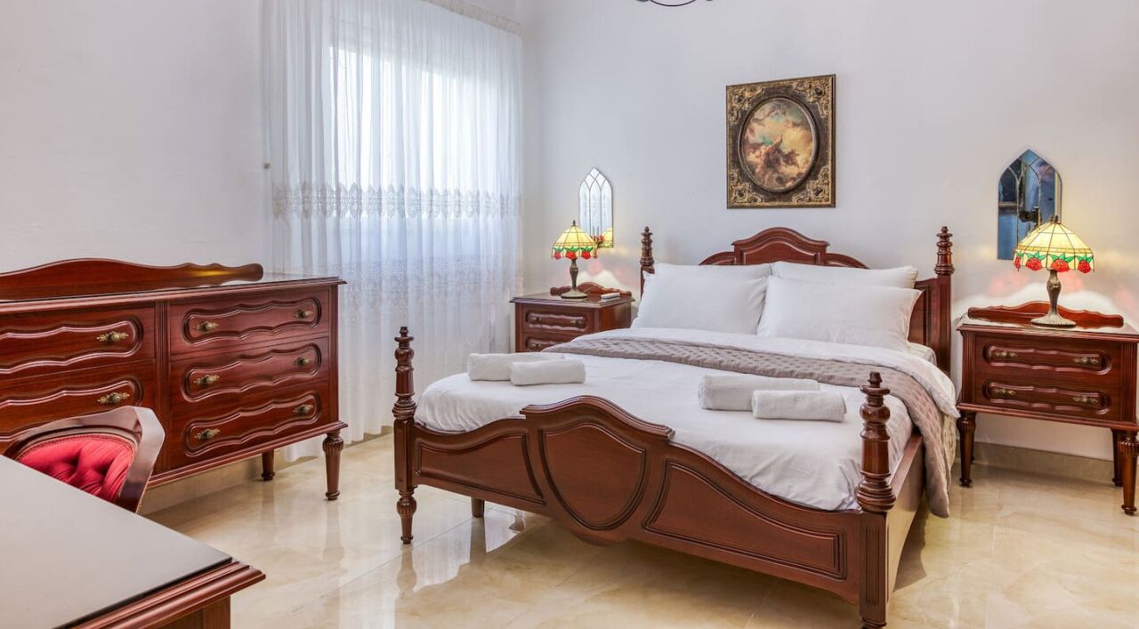 A bedroom with a wooden bed, two bedside tables with lamps, a dresser, and a painting on the wall.