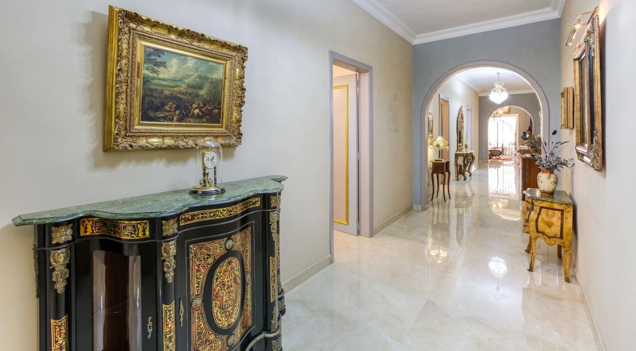 A hallway with a marble floor, ornate black and gold furniture, and framed artwork on the walls.