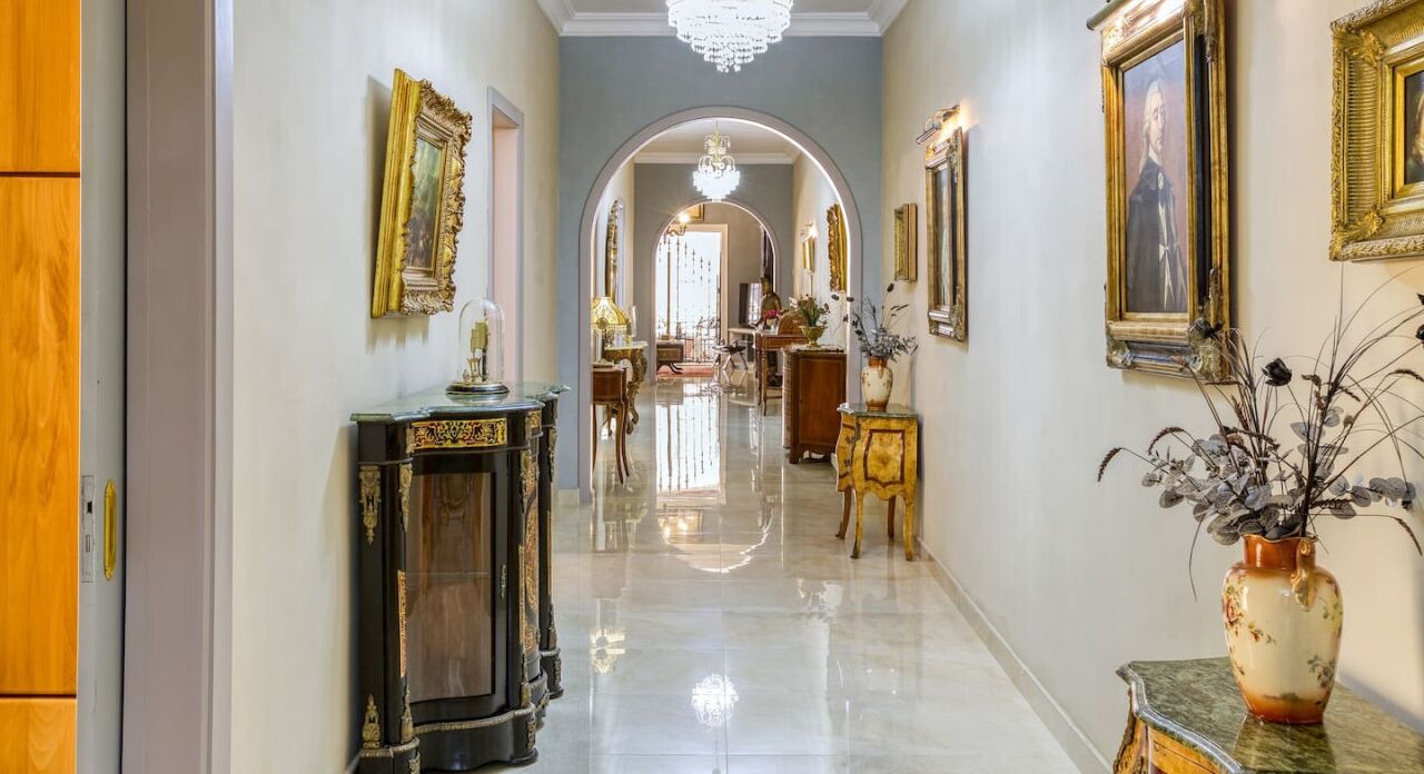 A hallway with ornate furniture, a chandelier, and framed artwork on the walls.