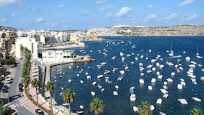 Un paysage urbain côtier avec un port de plaisance rempli de bateaux, des bâtiments le long du littoral et un ciel dégagé.