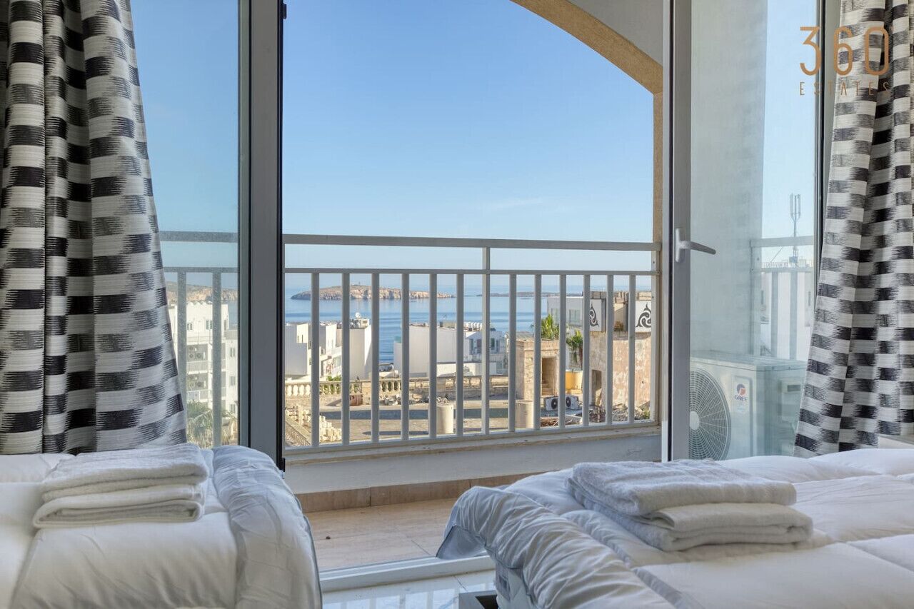 Een hotelkamer met een groot raam met uitzicht op een stadsbeeld en de zee.