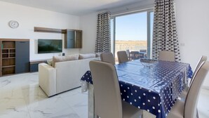 Un salon moderne comprenant un canapé, une table à manger avec des chaises, un téléviseur et une grande fenêtre avec des rideaux.