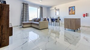 Un salon moderne avec un canapé d’angle, un meuble en bois et un coin repas comprenant une table et des chaises.