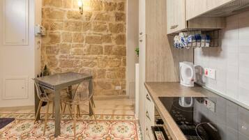 A kitchen with a stone wall, a table with chairs, a kettle, and a built-in oven.
