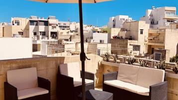 A rooftop terrace with outdoor furniture, a large umbrella, and a view of a densely packed urban area.