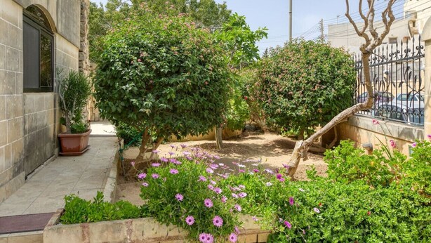 Une cour avec un bâtiment en pierre, des plantes en pot et des arbustes en fleurs.