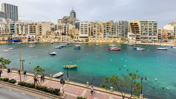 A marina with boats, a pedestrian walkway, and buildings in the background.