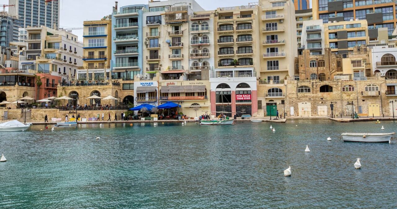 A waterfront area with buildings, a marina, and a restaurant with outdoor seating.