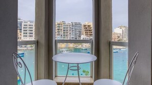 A balcony with two metal chairs and a small round table, overlooking a marina and buildings.