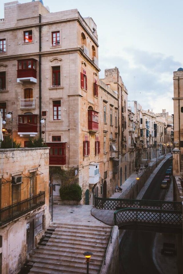 Une rue étroite bordée de bâtiments historiques aux volets rouges et aux balcons, qui mène à un escalier.