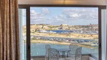 Een balkon met een tafel en stoelen, met uitzicht op een jachthaven met boten en een verre skyline.