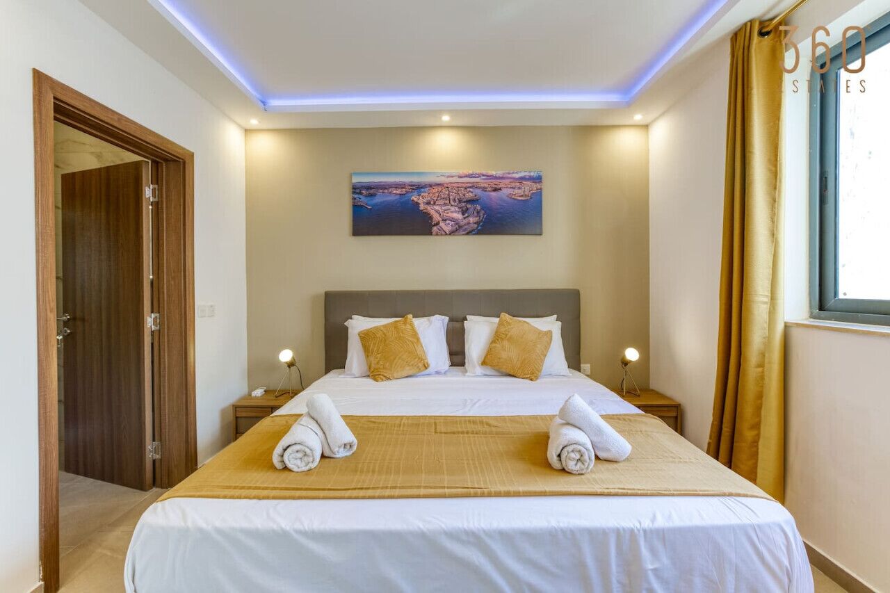 Une chambre d’hôtel avec un grand lit, deux tables de chevet, un tableau au mur et une vue sur la mer.