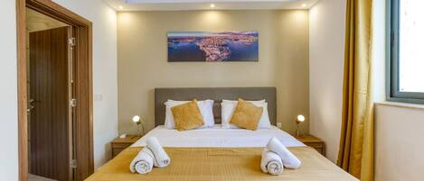 Une chambre d’hôtel avec un grand lit, deux tables de chevet, un tableau au mur et une vue sur la mer.