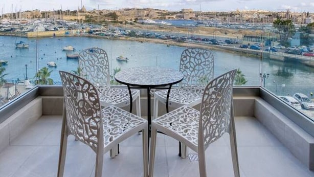A balcony with two chairs and a table, overlooking a marina with boats and a distant cityscape. - Lovely Waterfront Apt with Stunning Views in Gzira (Il-Gżira)
