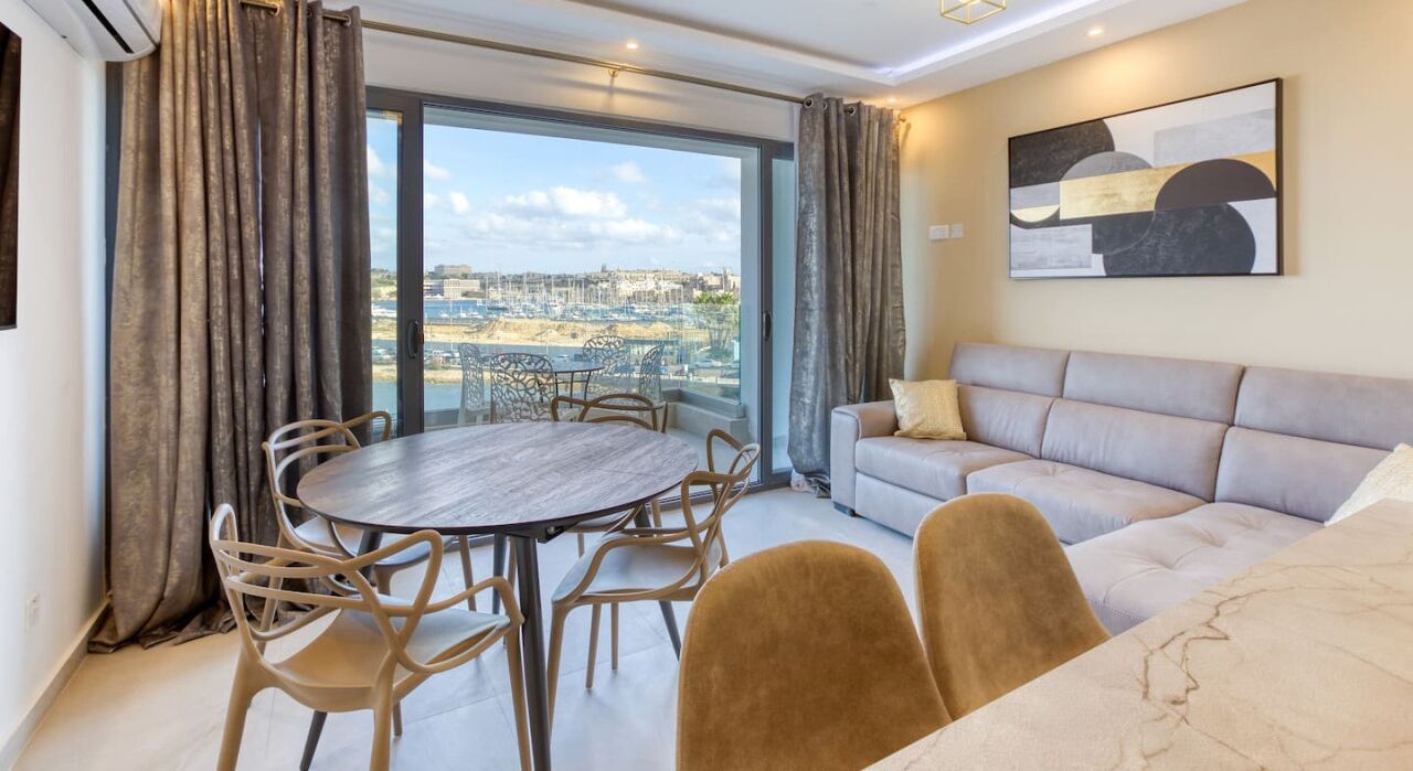 Een moderne woonkamer met een ronde tafel en stoelen, een bank en een groot raam met uitzicht op de stad.