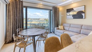 A modern living room with a round table and chairs, a sofa, and a large window with a city view. - Lovely Waterfront Apt with Stunning Views in Gzira (Il-Gżira)