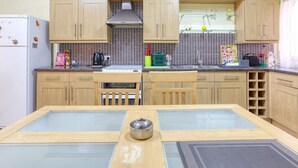 A kitchen with wooden cabinets, a refrigerator, a stove, and a dining table with chairs. - Charming 2BR Apt with Cosy Balcony in Marsascala (Wied il-Għajn)