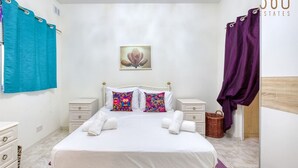 A neatly arranged bedroom with a bed, two pillows, a nightstand, a basket, and a purple curtain. - Charming 2BR Apt with Cosy Balcony in Marsascala (Wied il-Għajn)