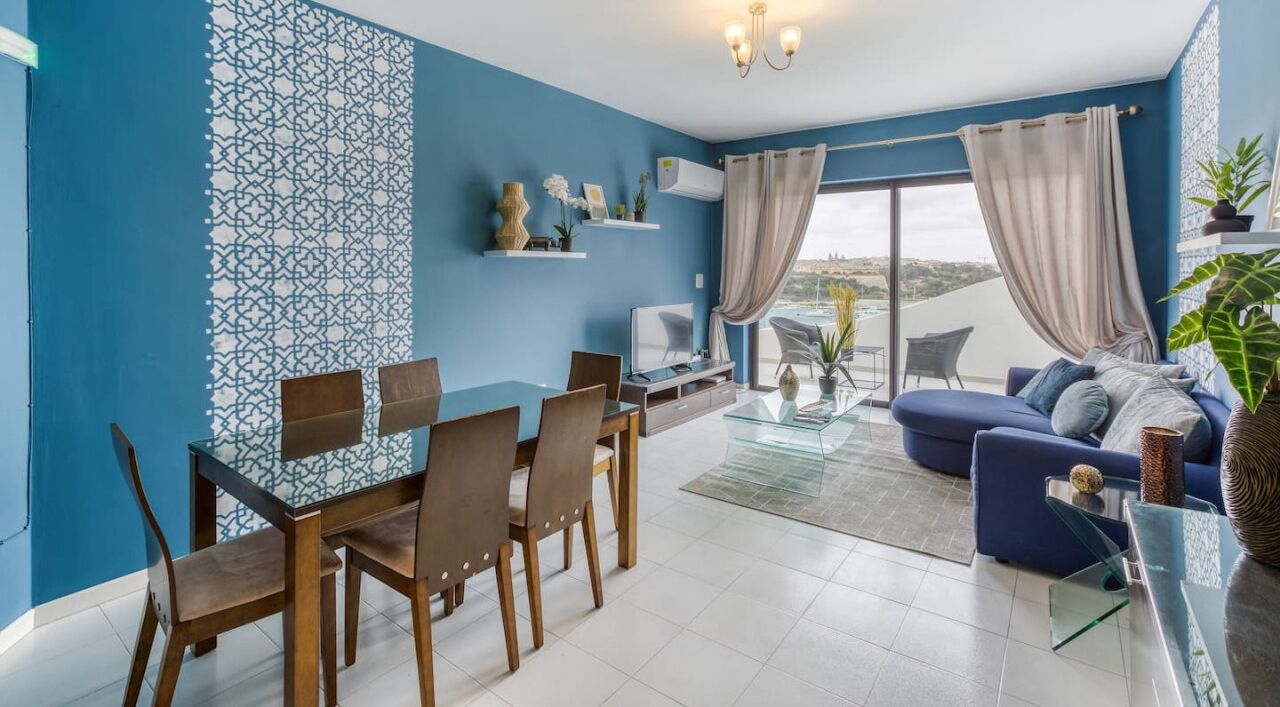 Ein modernes Wohnzimmer mit blauer Akzentwand, einem Essbereich mit Holzmöbeln und einem Sofa mit Aussicht.