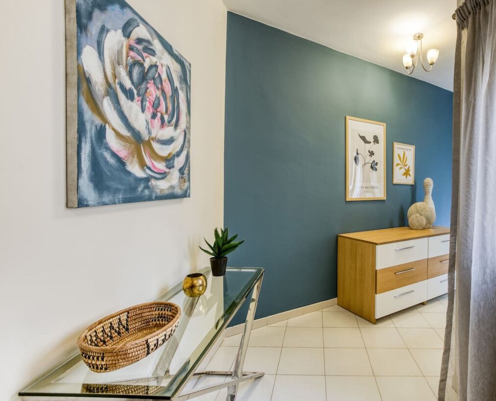 Un salon moderne avec un mur d’accent bleu, une table basse en verre, un meuble en bois et une estampe botanique encadrée.