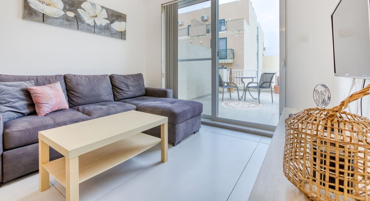 Una sala moderna con un sofá gris, una mesa de centro de madera y una cesta de mimbre.