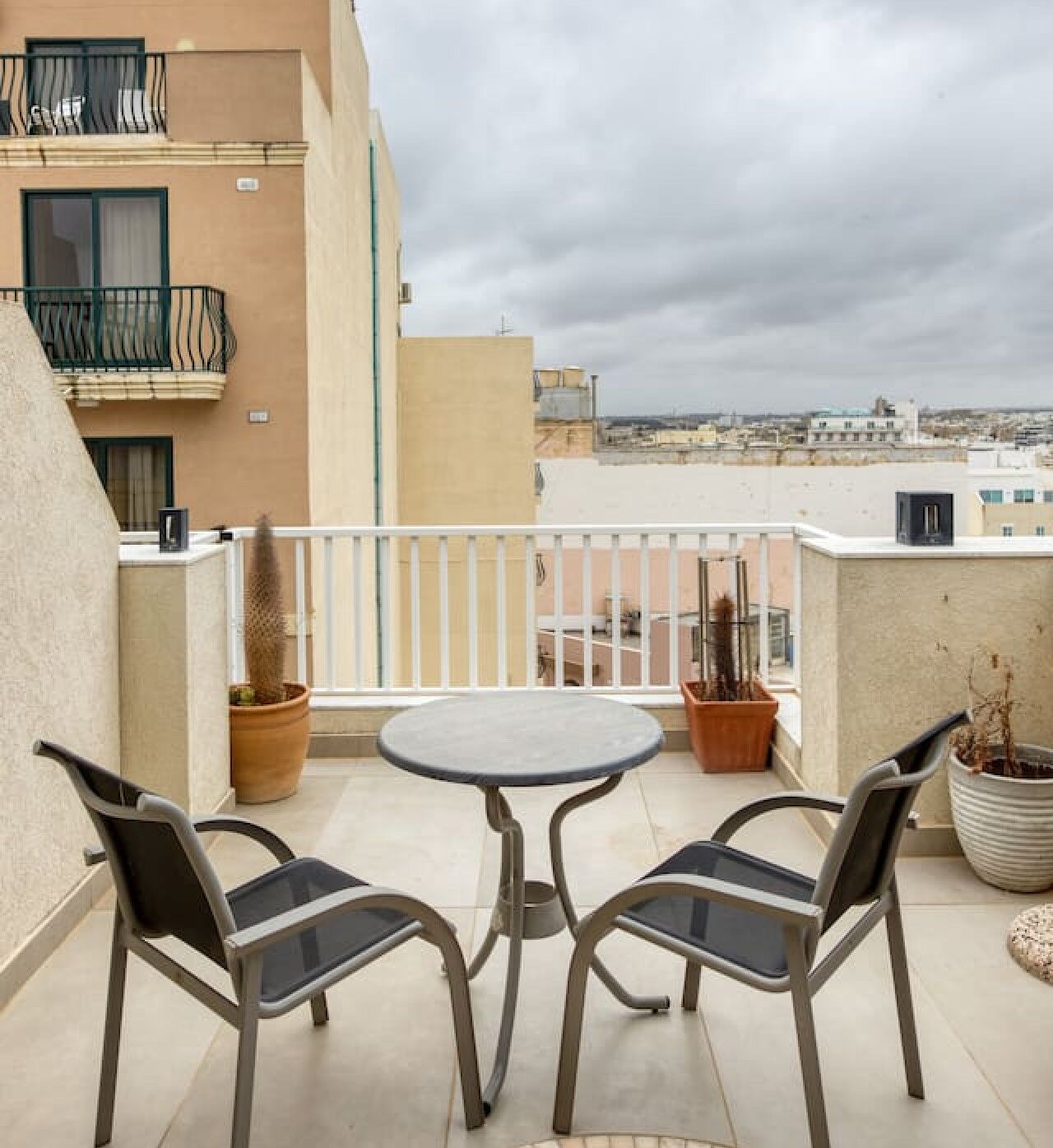 Een balkon met een ronde tafel en twee stoelen, potplanten en uitzicht op de stadsgezicht.