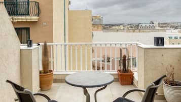Een balkon met een ronde tafel en twee stoelen, potplanten en uitzicht op de stadsgezicht.