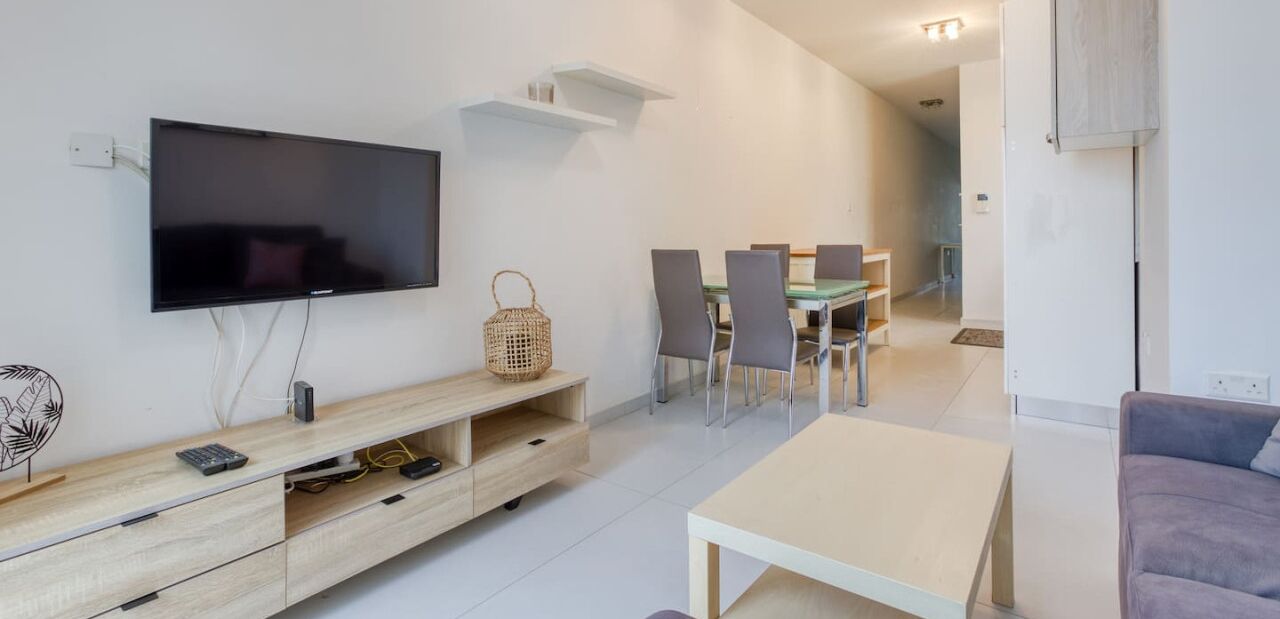 En moderne stue med et fladskærms-tv på væggen, et træunderholdningsmøbel, et spisebord med stole og en sofa.