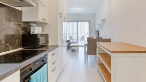 A modern kitchen with a built-in stove, oven, and microwave. There is a dining area with a table and chairs visible in the background. - Cosy 1BR penthouse with Private Terrace in Gzira (Il-Gżira)