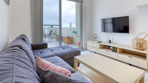 A modern living room with a grey sofa, a wooden coffee table, a TV, and a balcony with a view of the city. - Cosy 1BR penthouse with Private Terrace in Gzira (Il-Gżira)