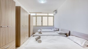 Quarto com duas camas, um guarda-roupa e uma janela que ilumina naturalmente.