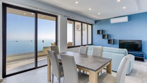 Uma sala de estar moderna com uma grande porta de vidro deslizante para uma varanda, uma televisão de tela plana e uma área de jantar com mesa e cadeiras.