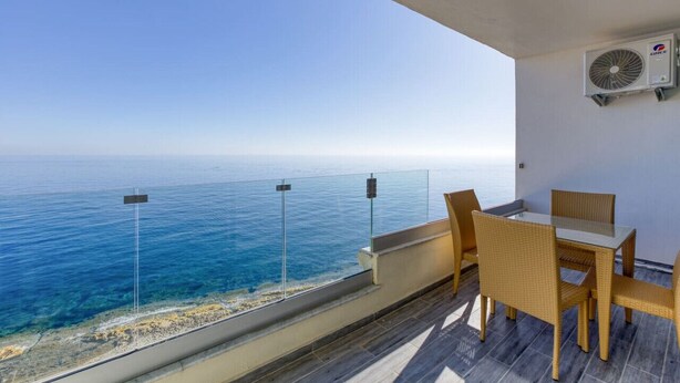 Varanda com mesa e cadeiras, vista para o mar.