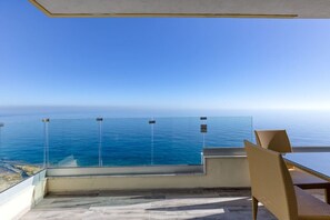 Un balcon offrant une vue dégagée sur l’océan, une table en verre et des chaises en osier.