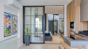 Una cocina moderna con horno empotrado, un comedor con mesa de vidrio y una escalera que sube a un dormitorio tipo loft.