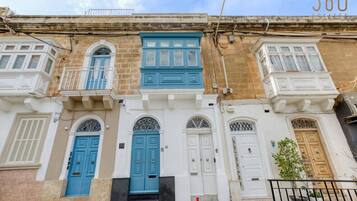 A row of traditional Mediterranean-style buildings with blue and white doors, balconies, and a clear sky.